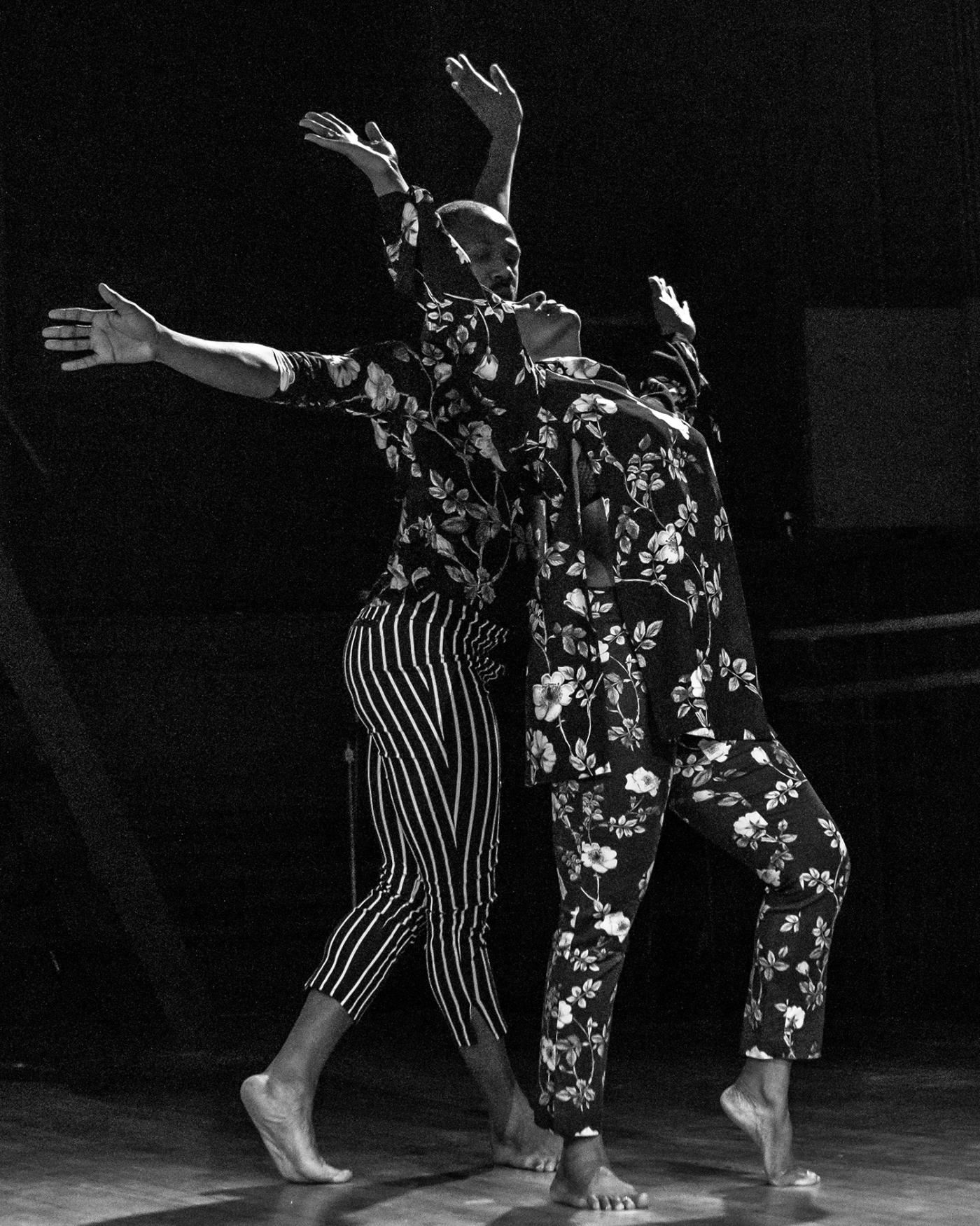 In black and white, two Black dancers perform in floral costumes.