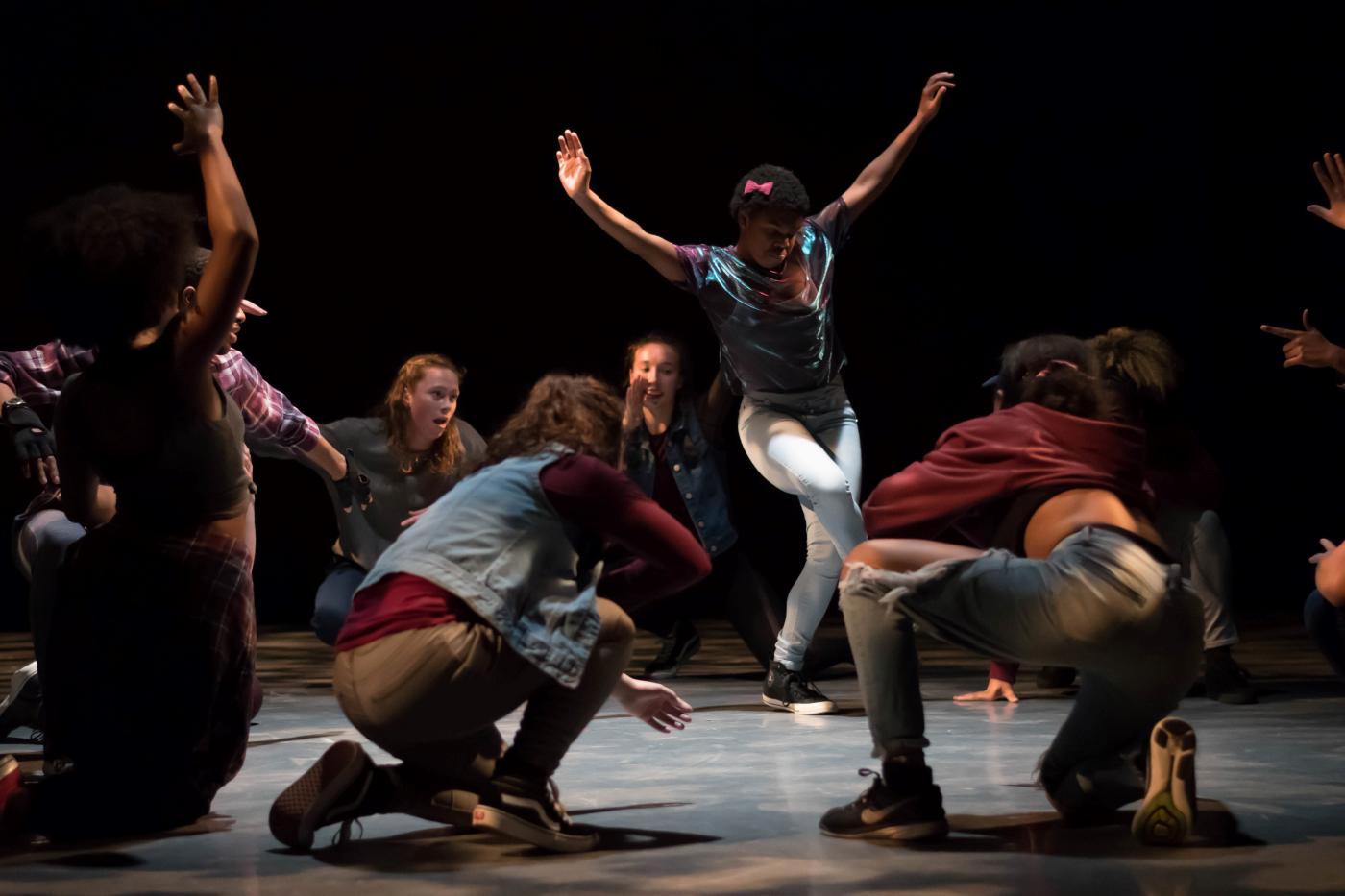 In a spotlight, a group of young dancers performs in a circle.