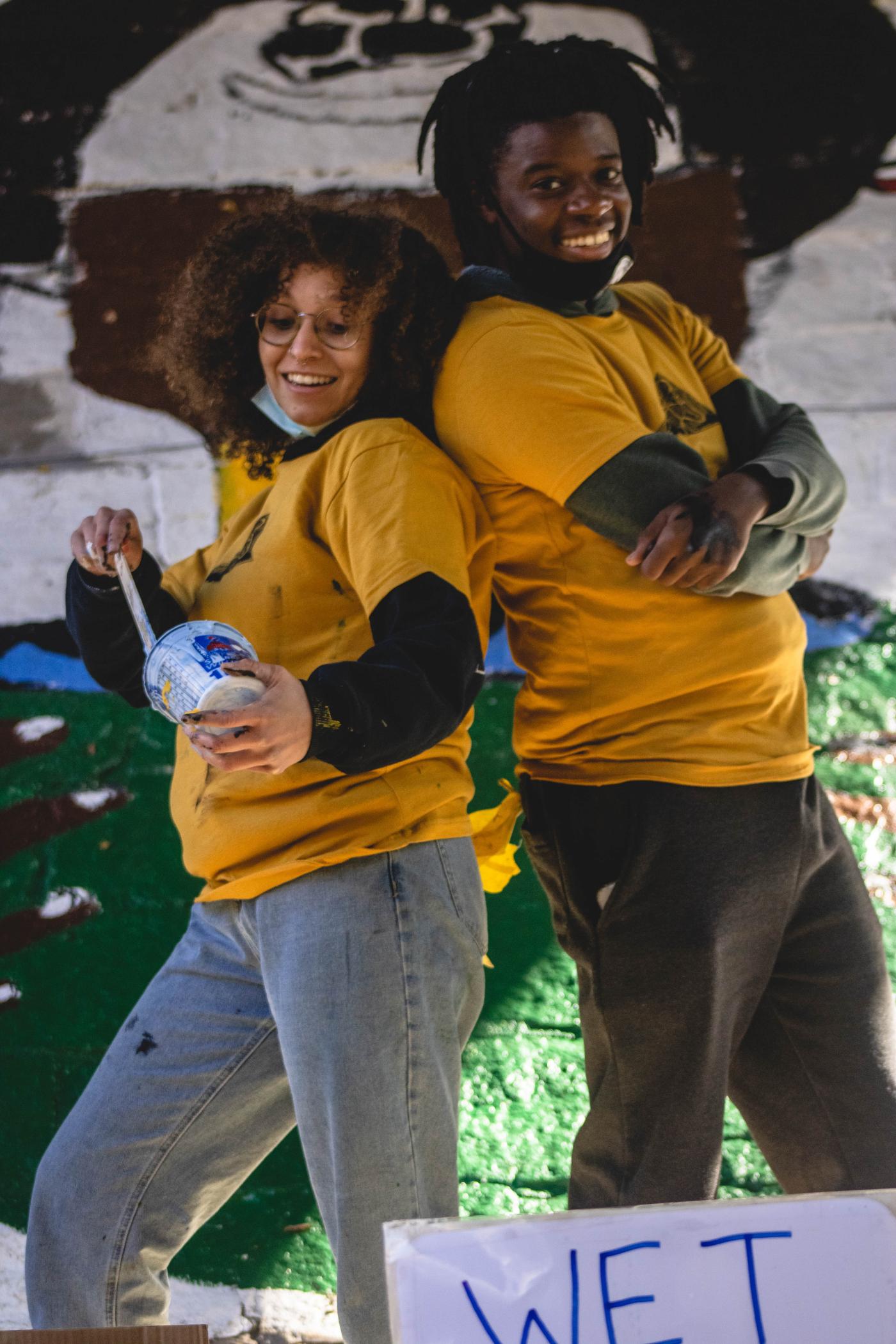 Two folks pose back to back in their matching yellow t-shirts.