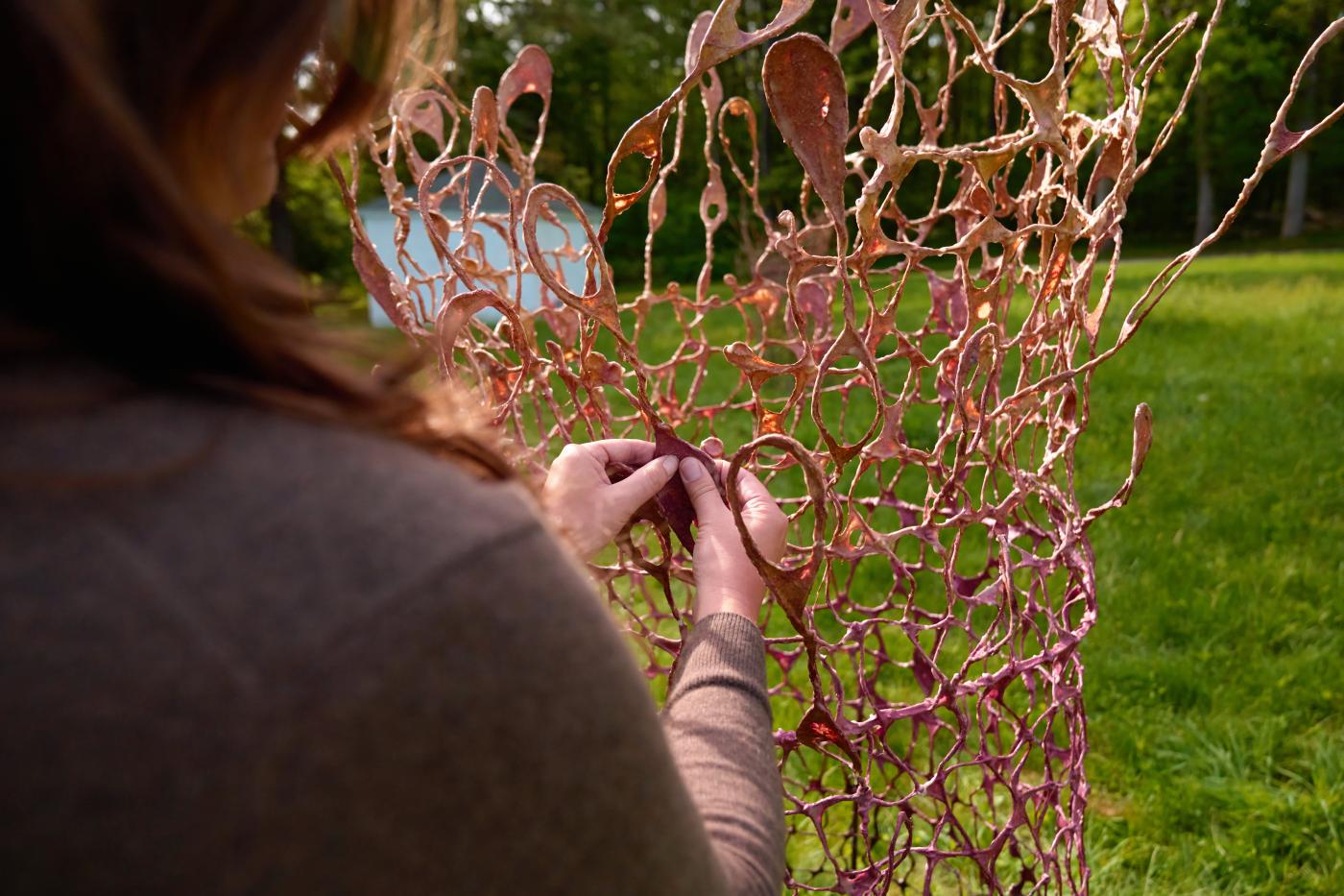 In grassy field, a closeup of a woman's hands braiding paper netting.