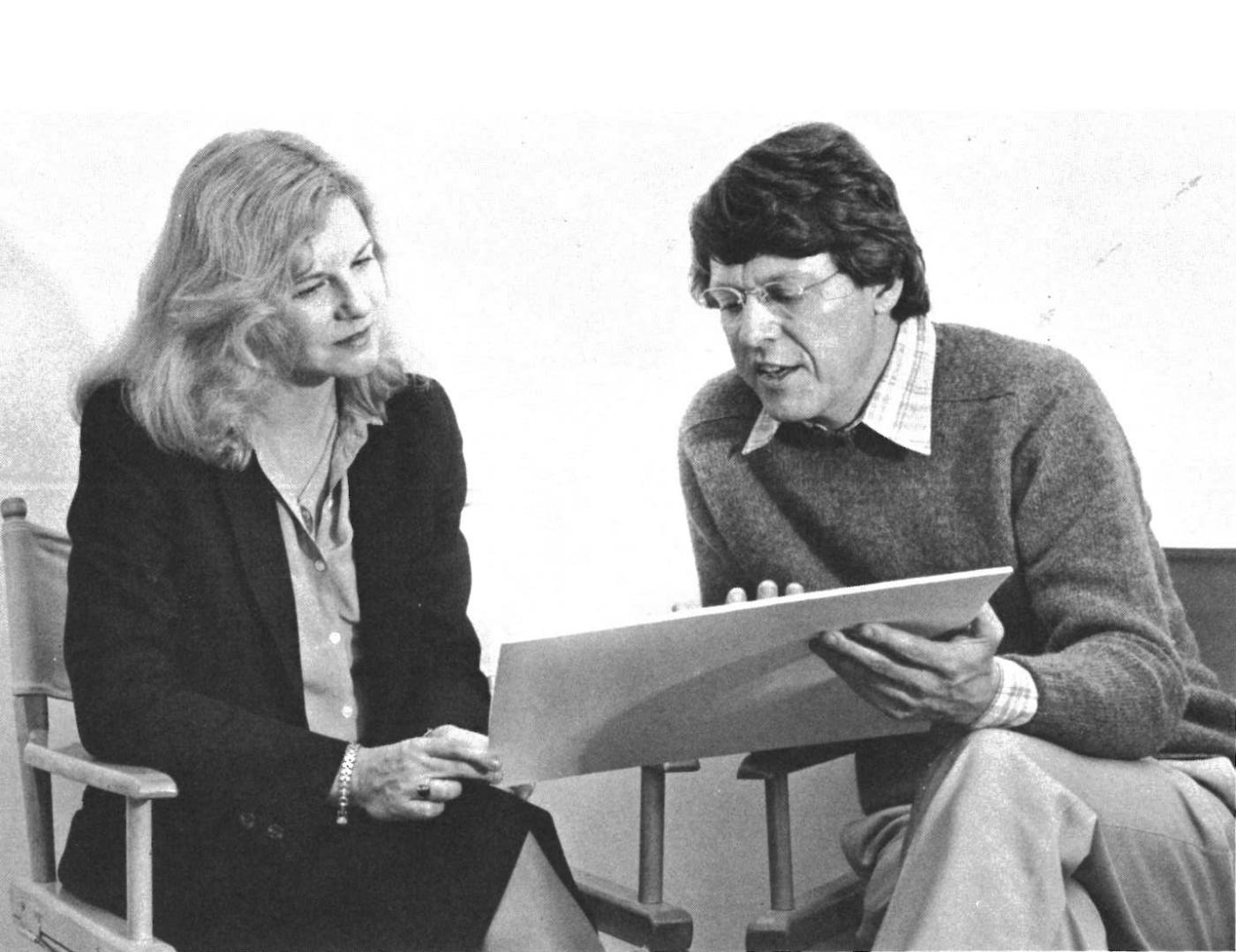 A white woman and a white man, in business casual, look at a printed document together.