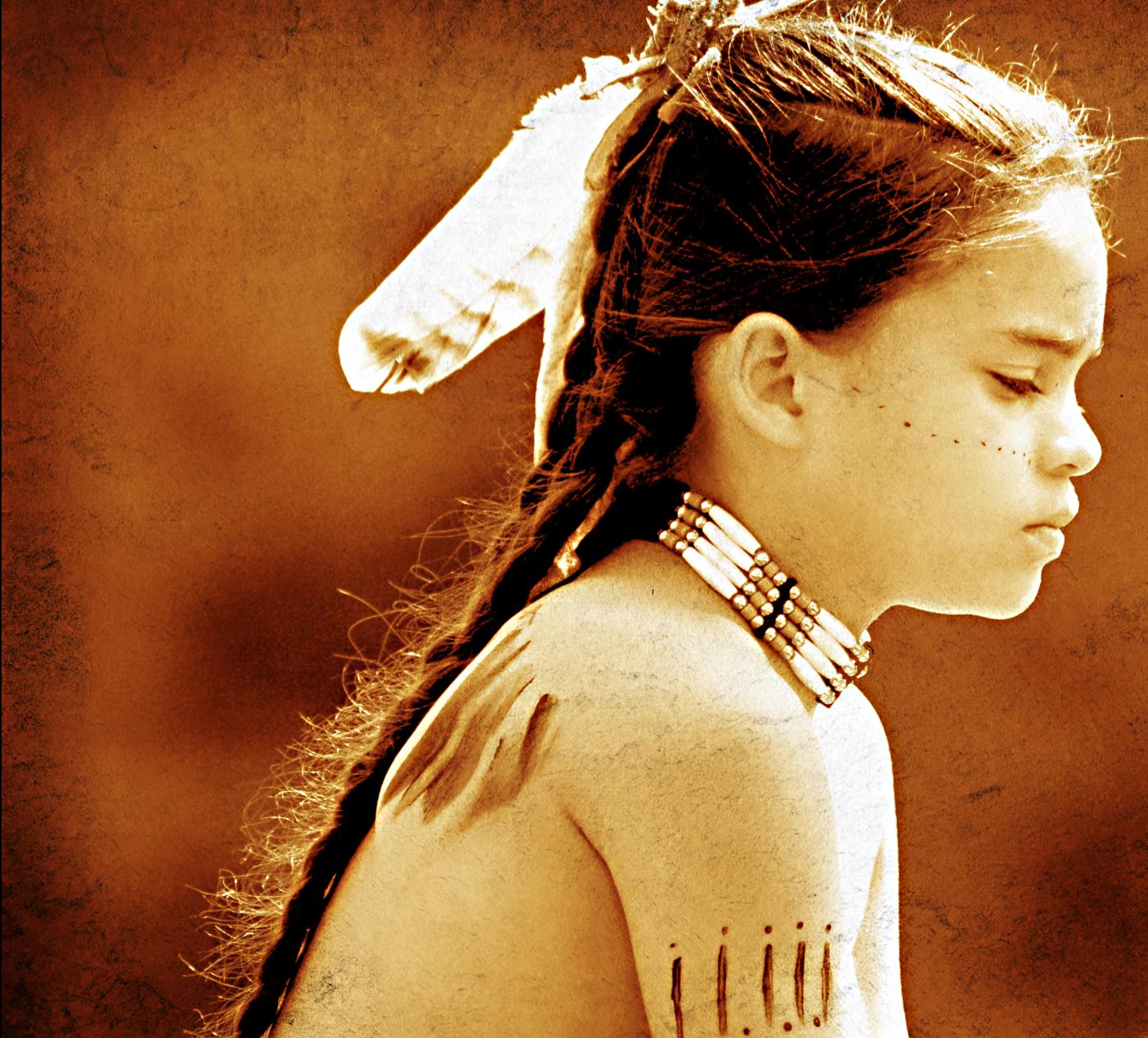 A young boy wears a feather in her braid, a beaded choker, and body paint.