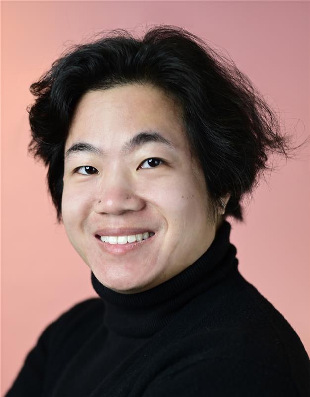 Llewellyn has hair that hits at his cheek bones. He wears a black turtleneck in front of a peach backdrop.