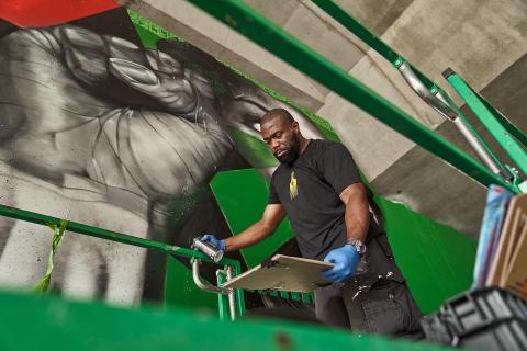 Rob works on a green lift. Next to him is a mural of a fist.