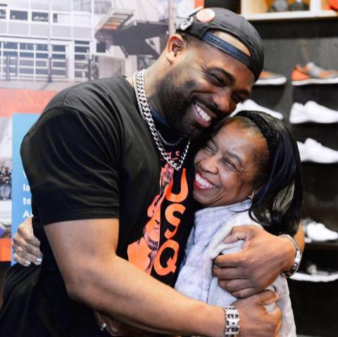 A Black man (Rob) in a backwards baseball cap and graphic tee hugs an older Black woman.