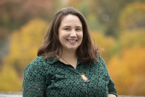 Woman outside smiles in front of autumnal trees