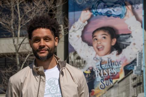 Marquis poses in front of a mural of a young girl holding an hourglass.