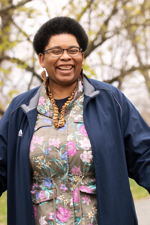 Catherine wears a floral shirt and navy jacket. She has chunky jewelry and smiles wide.