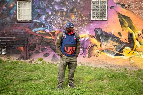 Next to a brick building with a galaxy mural, Rob looks right with his face obscured by his hat.