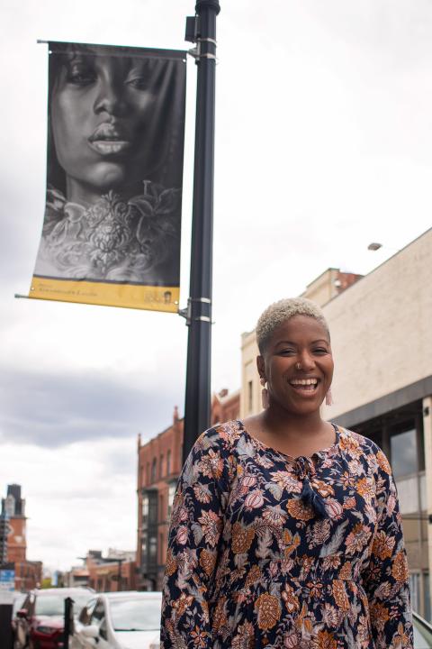 Christa poses next to a post with a flag of a painting of a Black women affixed to it.