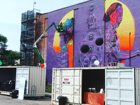 A predominantly purple mural with a setting sun next to some silhouettes.