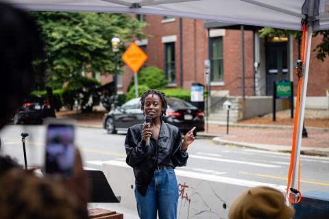On a street, a Black woman leads a tour group with a microphone.
