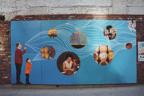 On the side of a brick building, a mural of an Asian man and child blowing bubbles that have images inside of them.