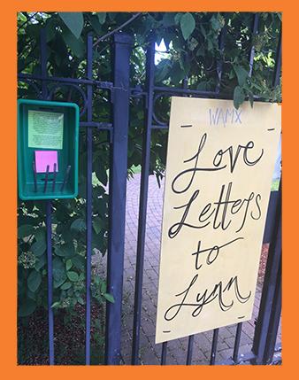On a black metal fence, a box hangs next to a sign that reads "Love Letters to Lynn."