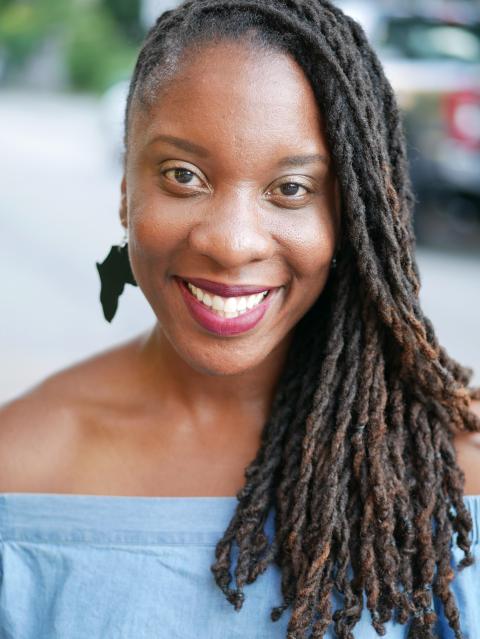 Aysha is a Black woman with long braids and a big beautiful smile.