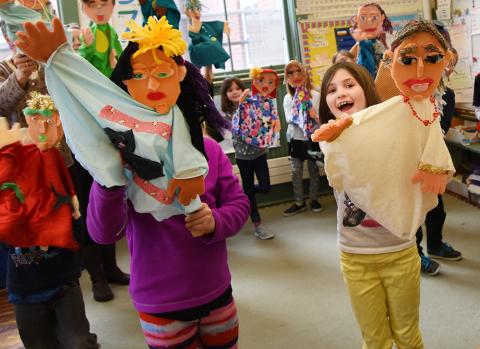 A group of colorfully dressed children pose with the large cloth puppets they made in their images.