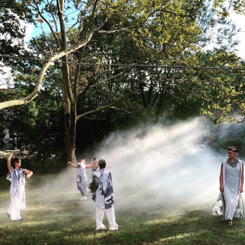 Dancers in a field walk around a fog forming in between them.