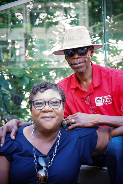 By some trees, an elderly, Black straight couple poses together. 