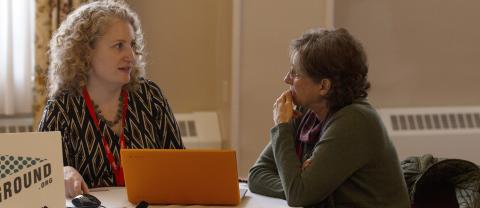 Two women talk to each other while looking at the same laptop