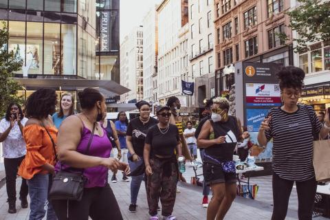 On a city street, folks dance in lines.