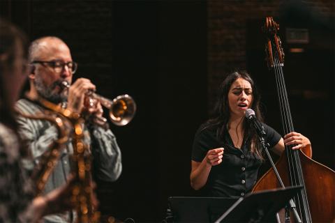 Mali sings and holds a bass next to a man who plays a brass instrument.