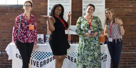 Four people stand in front of a table with CreativeGround materials, in a light airy space