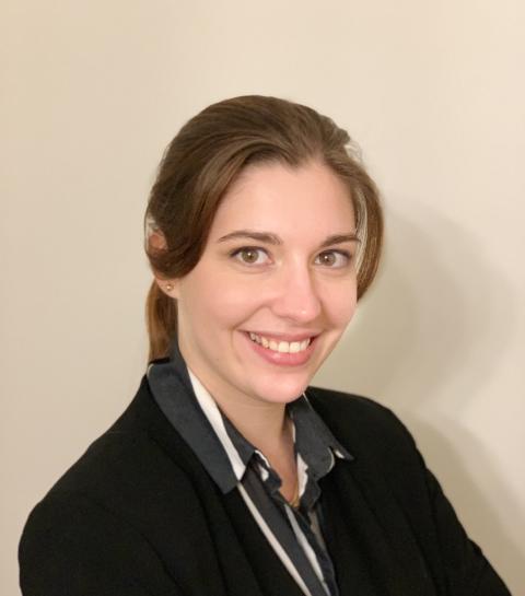 a woman with long hair pulled back wearing a black and white striped shirt and black blazer against a beige background