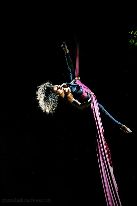 In a black void, a black woman with an afro gives an aerial performance with fabric.