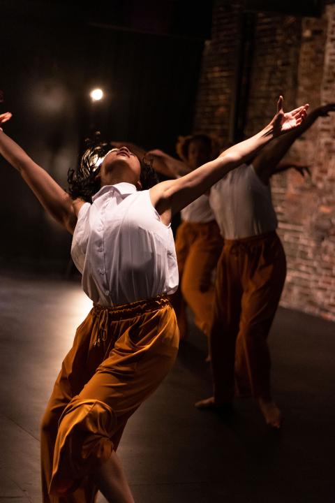 A dancer throws her arms up and leans to the side.