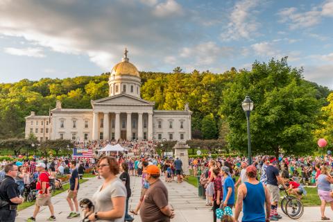 Image of a crowd of people on a warm sunny day with Vermont's capitol building in the background.