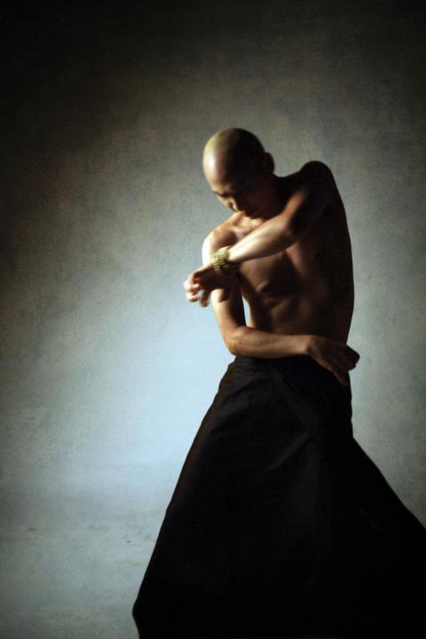 A dimly lit, shirtless dancer performs a butoh full body twist