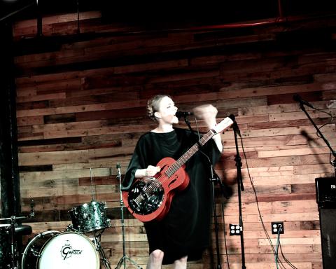 A white, female guitarist sings into a microphone