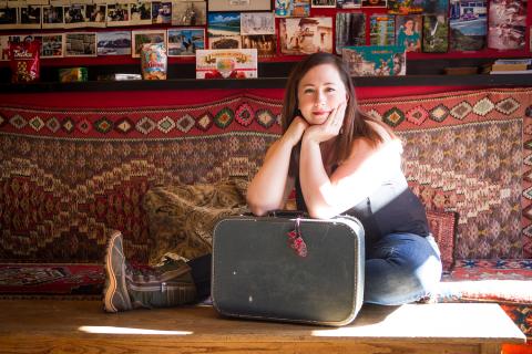 Sarah sits on the ground, leaning over a suitcase.