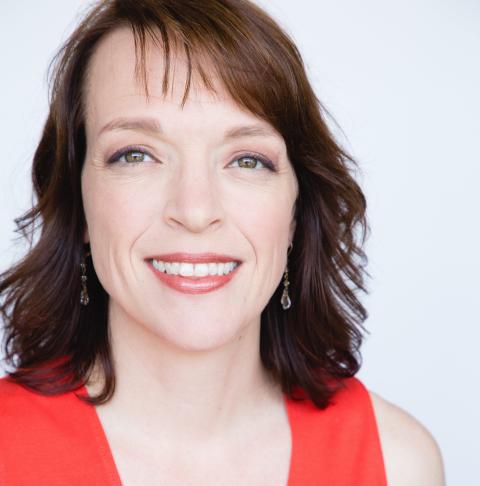 Sarah is a white woman with shoulder length reddish, brown hair. She smiles in front of a white backdrop.