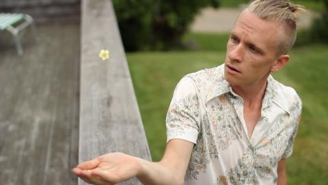 Scott holds his hand out to catch a flower. He has a blond bun.