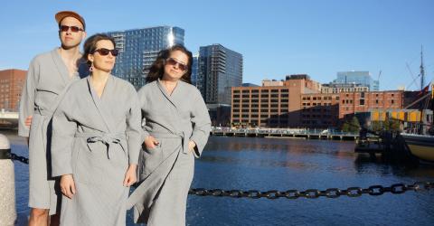 Two women and a man pose by a body of water in sunglasses and bathrobes.
