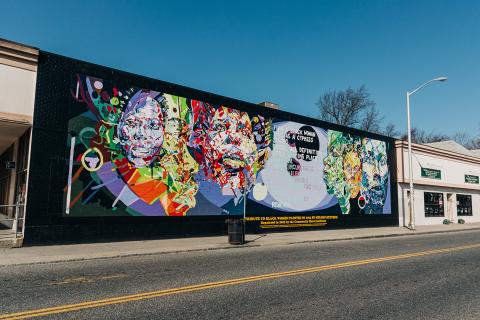 On the side of the building, a recreation of the portrait of Black women in human and neon hues. 