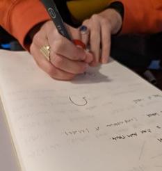 A pair of hands on a notebook; the right hand holds a pen and is making a note. 