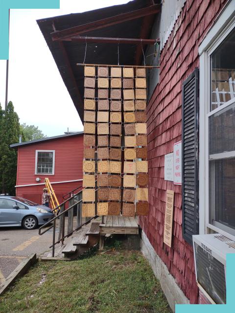 Brown wooden squares hang from a pole, on the side of a building with red shingles.