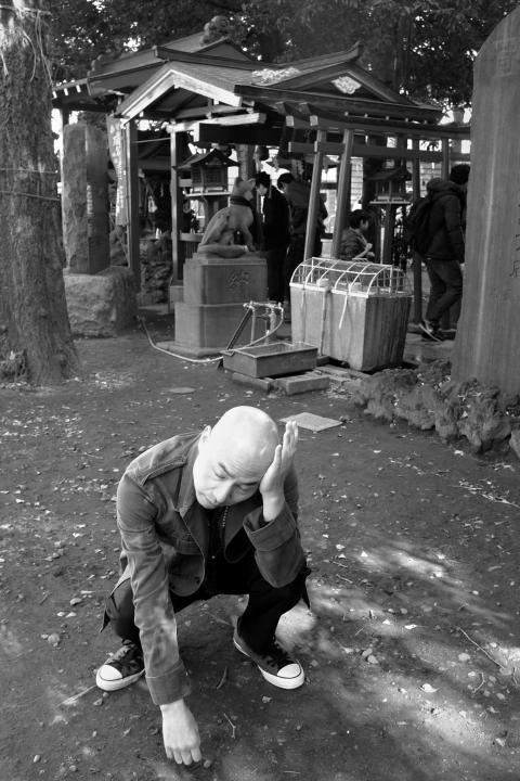Michael squats next to a Japanese shrine resting his head on his hand in a somewhat distraught emotion.
