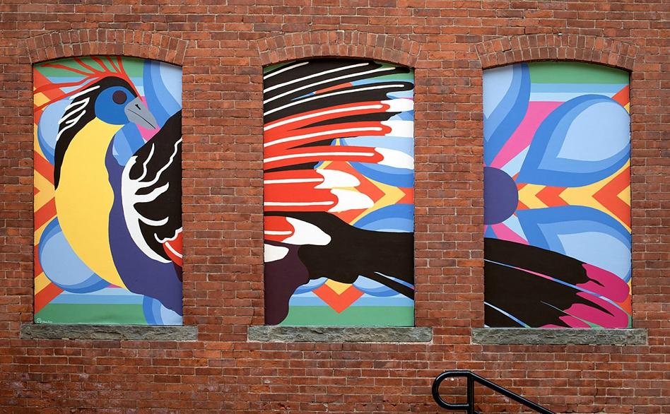 a colorful mural of a bird painted in three fake windows on a brick wall
