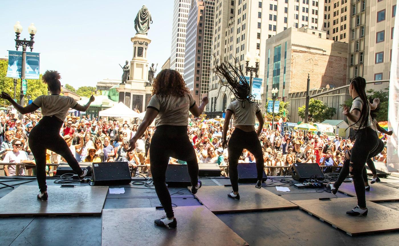 A group of steppers perform on an outdoor stage in front of a large crowd in downtown Providence