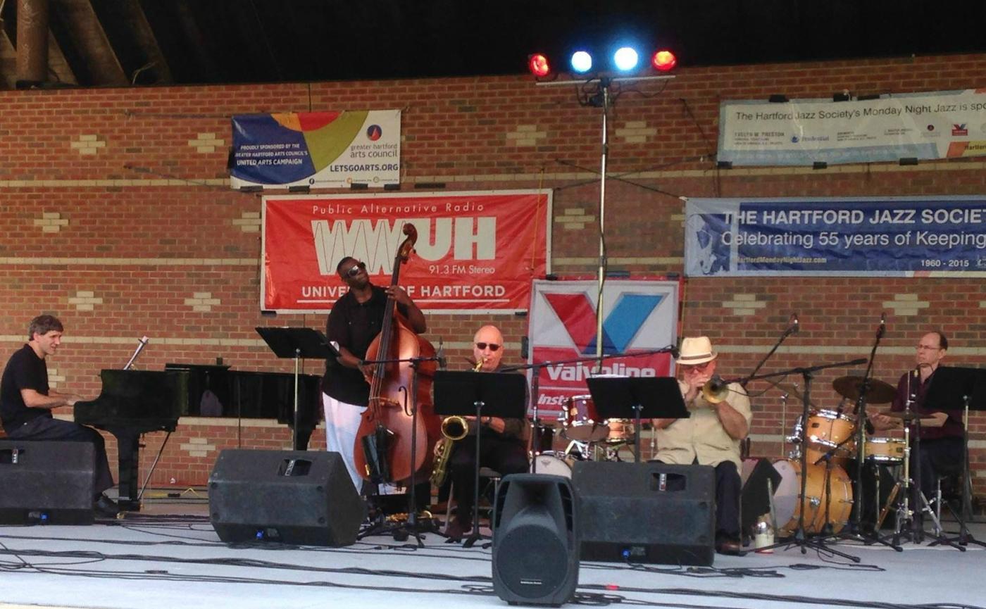 band members play jazz at an outdoor theater- piano, trumpet, bass, guitar