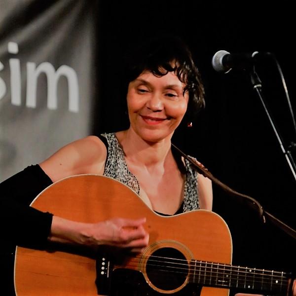 Thea plays a guitar and sings into a microphone at Club Passim music venue.