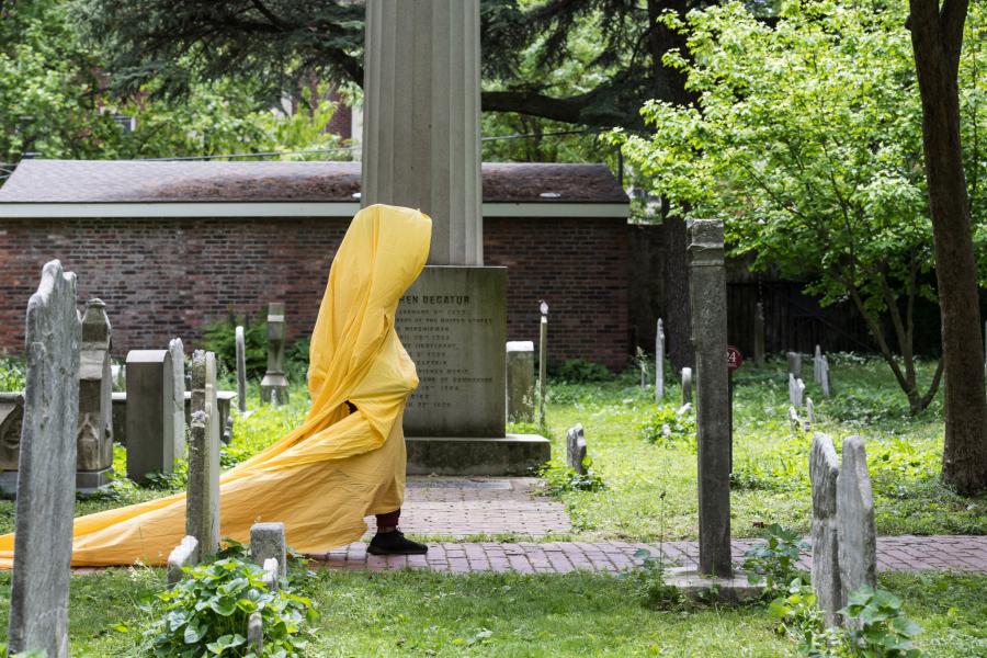 A person, wrapped in a yellow tarp, walks through a graveyard.