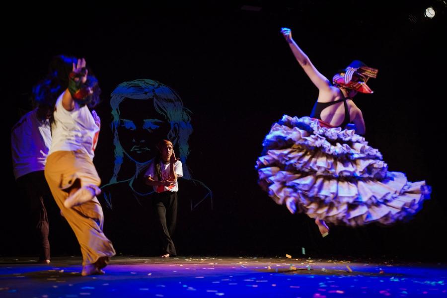 On a colorfully lit stage three performers dance in a triangle.