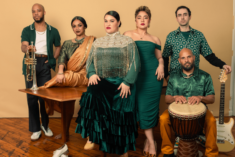 A group of six dressed in green pose in front of a mustard colored wall.