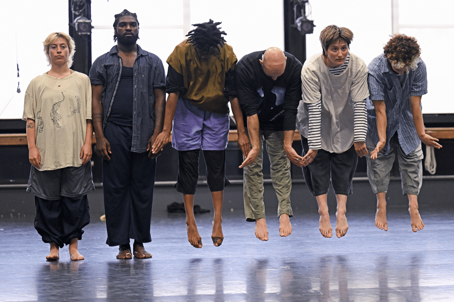 Six people are arrayed in a line, facing forwards. The two on the left stand straight while the other four are halfway through a hop, suspended in midair.