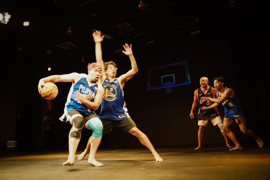Four people in athletic gear play basketballs indoors.