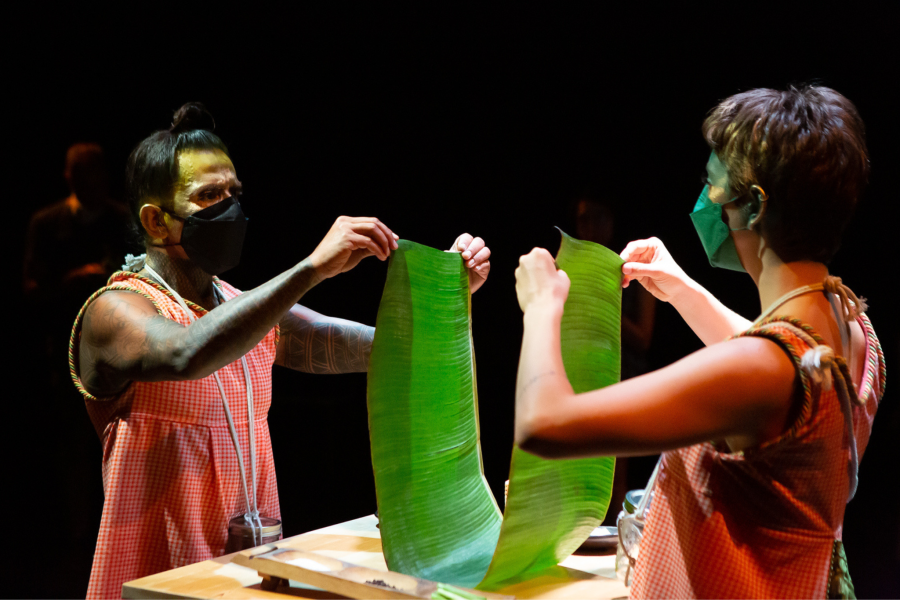 Two folks, in face masks, fold a long leafy green.